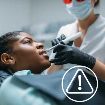 Dentist treating a patient using a handheld dental device during a procedure.